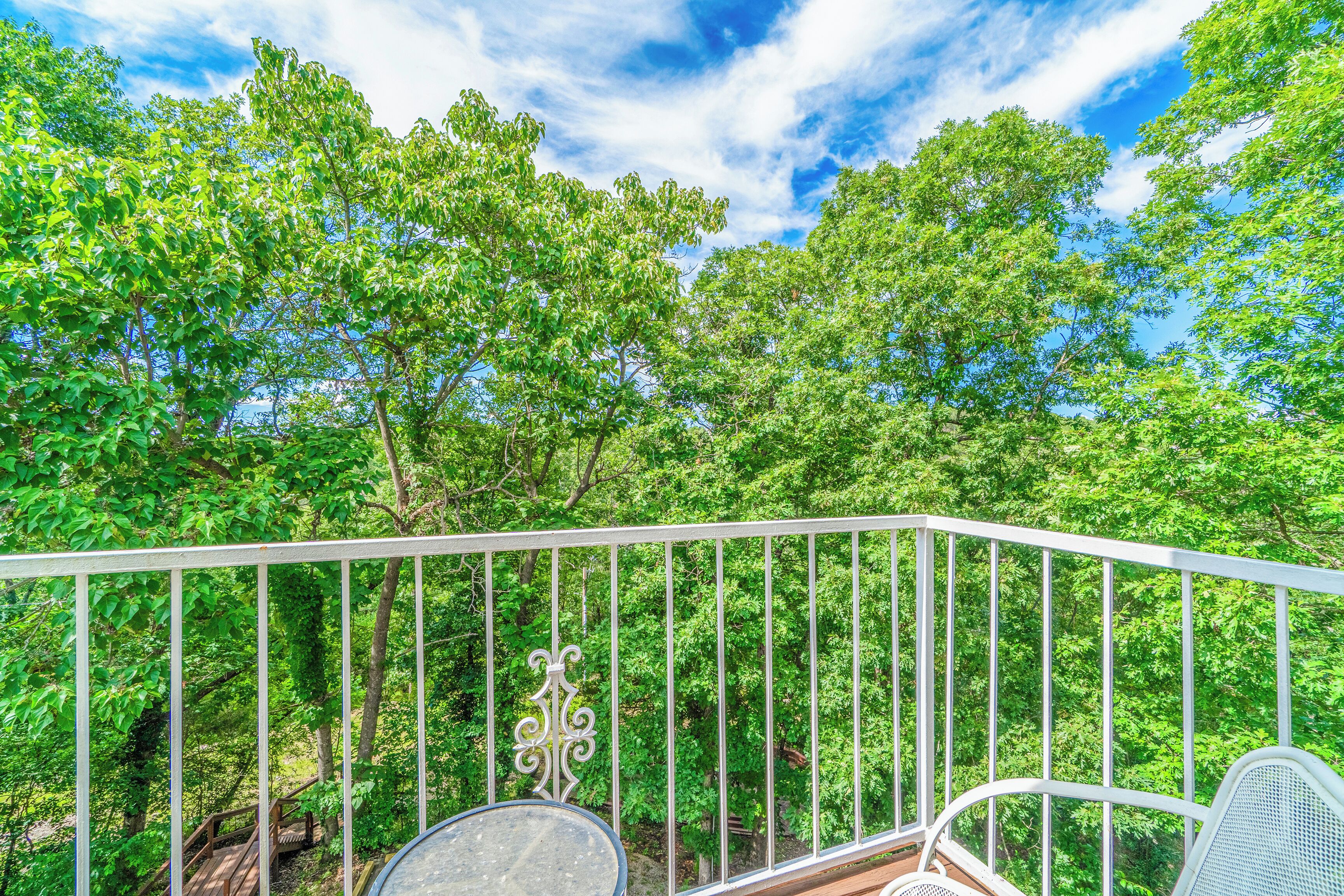 A balcony with a white railing, overlooking a lush green forest.