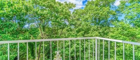 A balcony with a white railing, overlooking a lush green forest.