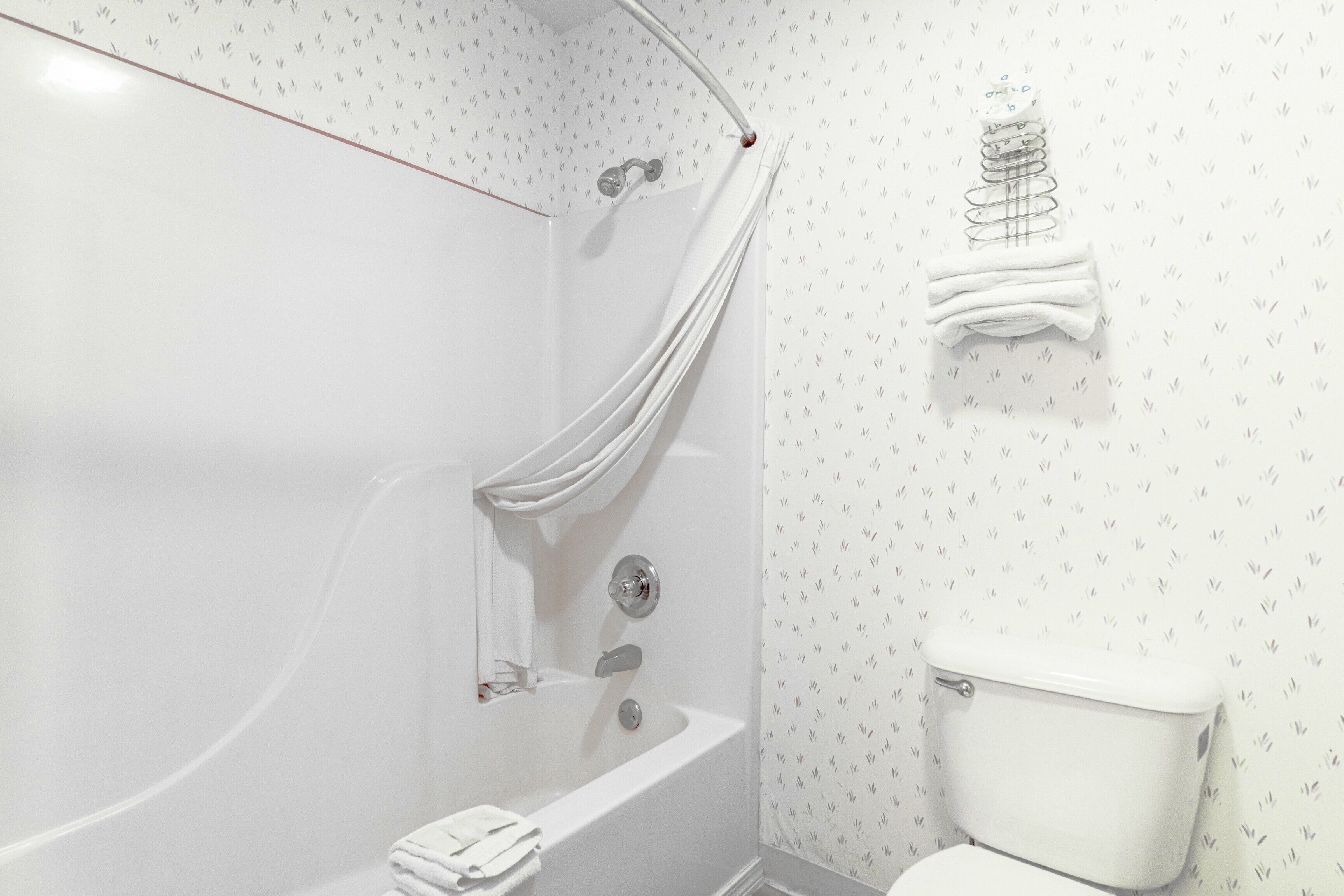 A bathroom with a bathtub, a shower curtain, a toilet, and a towel rack.