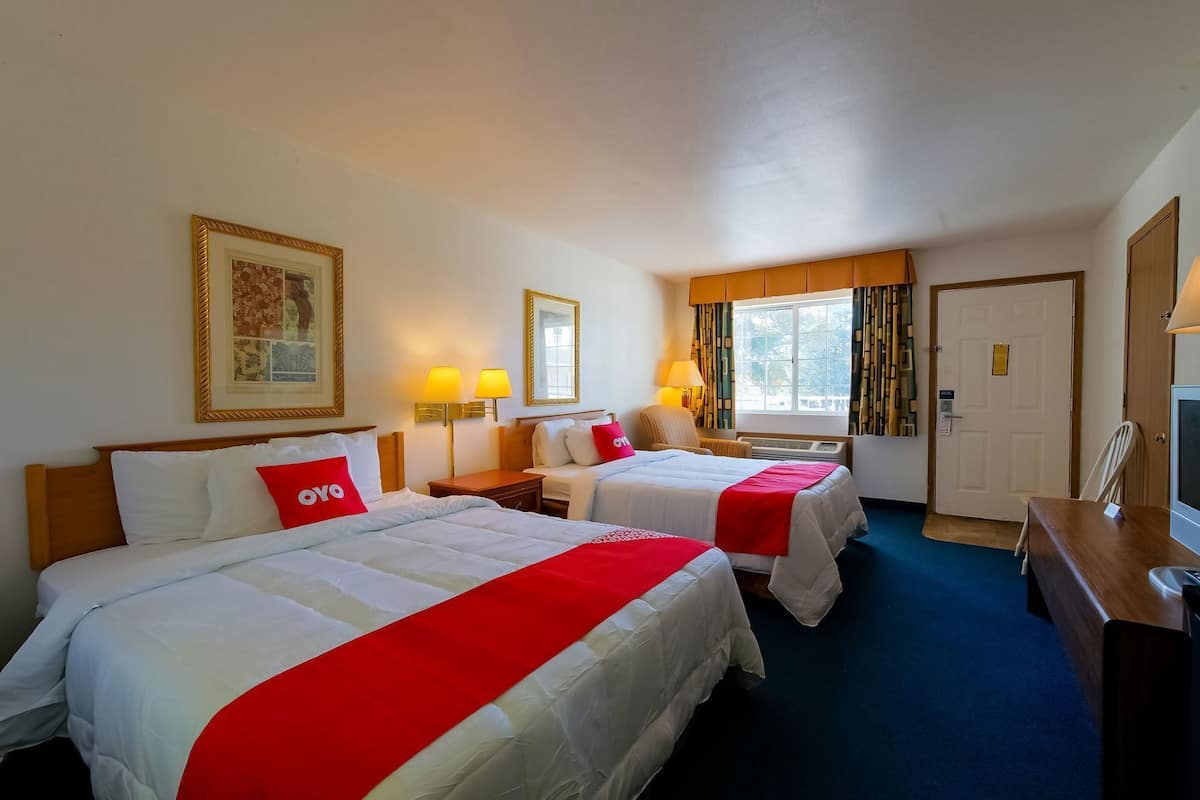 A hotel room with two beds, a desk, a TV, and a window with curtains.