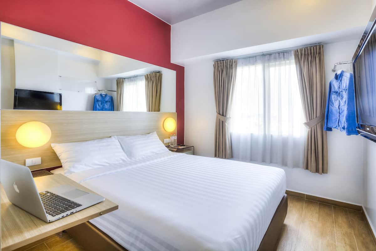 A hotel room with a bed, a desk with a laptop, a TV, and a mirror.