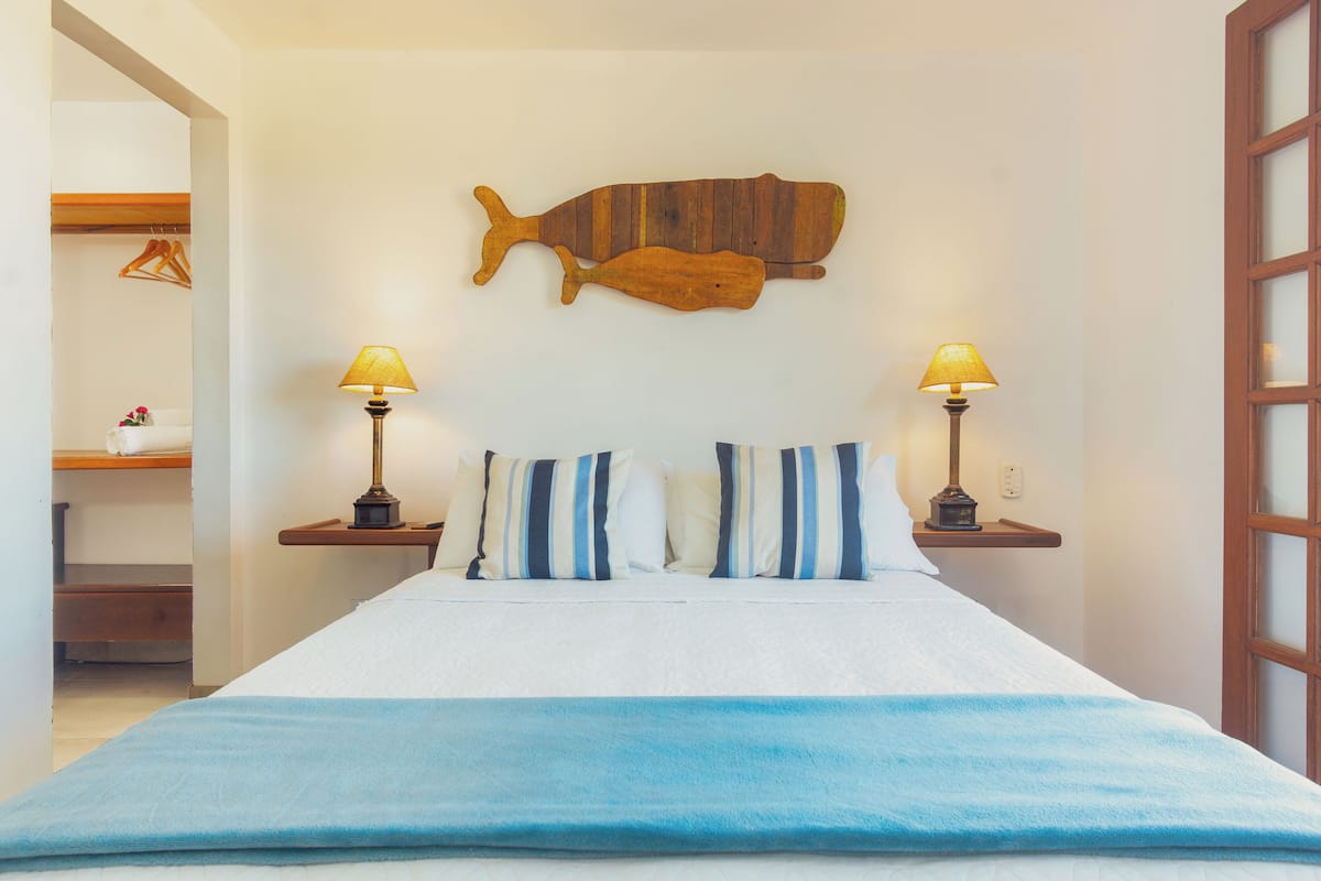 Ein Schlafzimmer mit einem Bett, gestreifte Kissen, zwei Nachttischlampen und einer Holzwandgestaltung mit Fischmotiven.