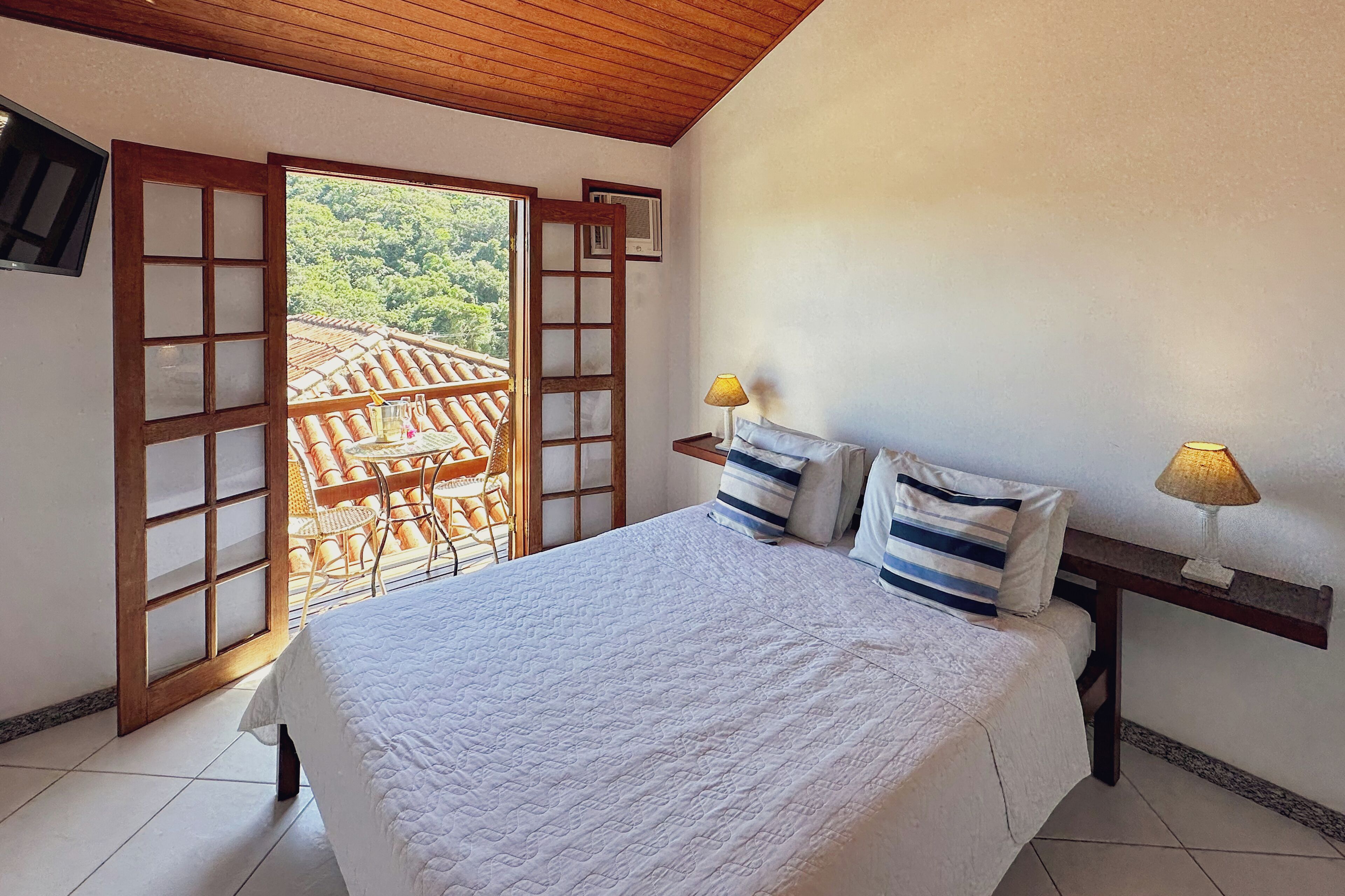 Un dormitorio con cama, dos lámparas de noche, una mesita de madera y vistas a una terraza con sillas y una mesa.