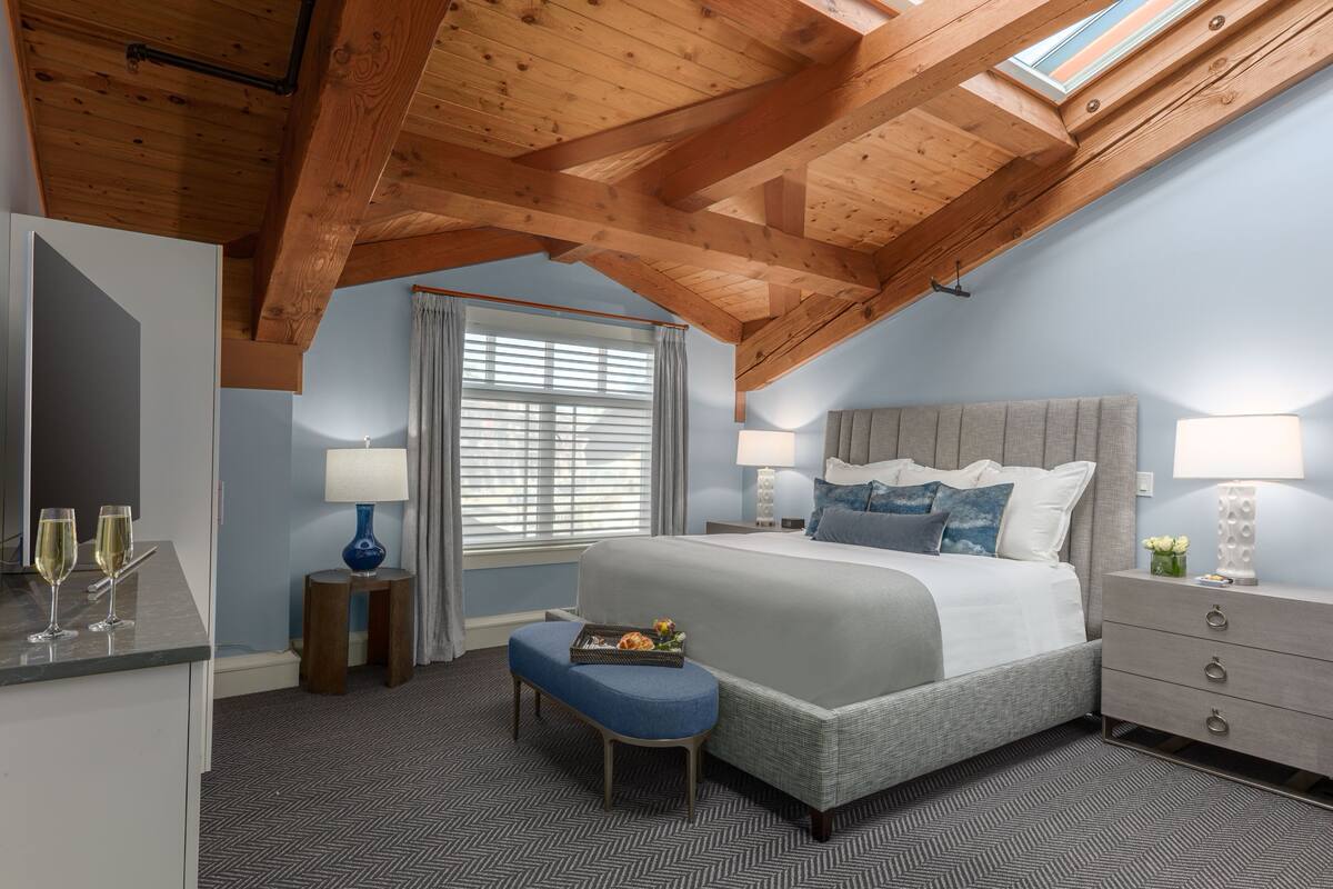 A bedroom with a large bed, a bench, a dresser, and a window with curtains.