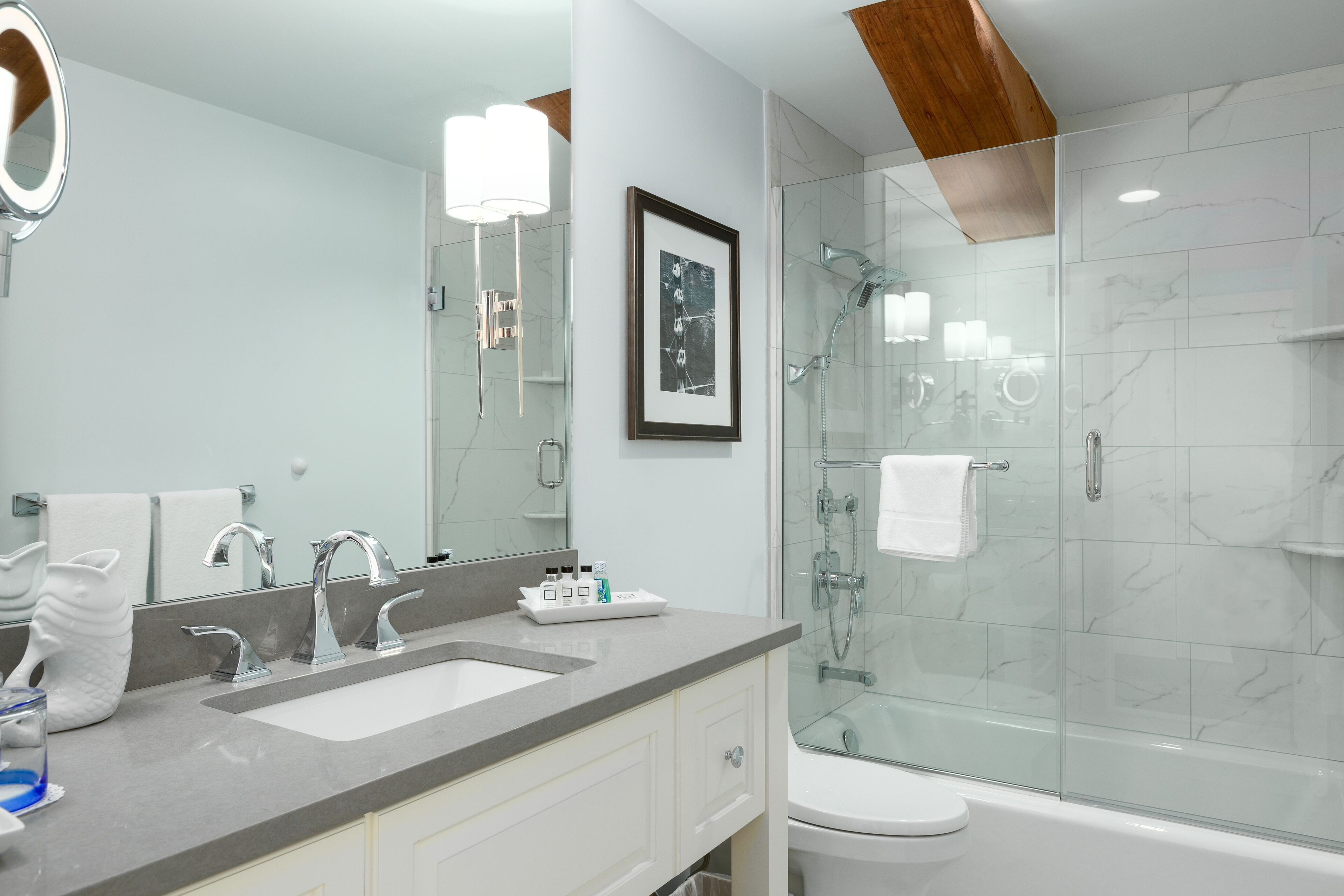 A modern bathroom with a dual sink vanity, a large mirror, a framed picture, and a glass-enclosed shower area.