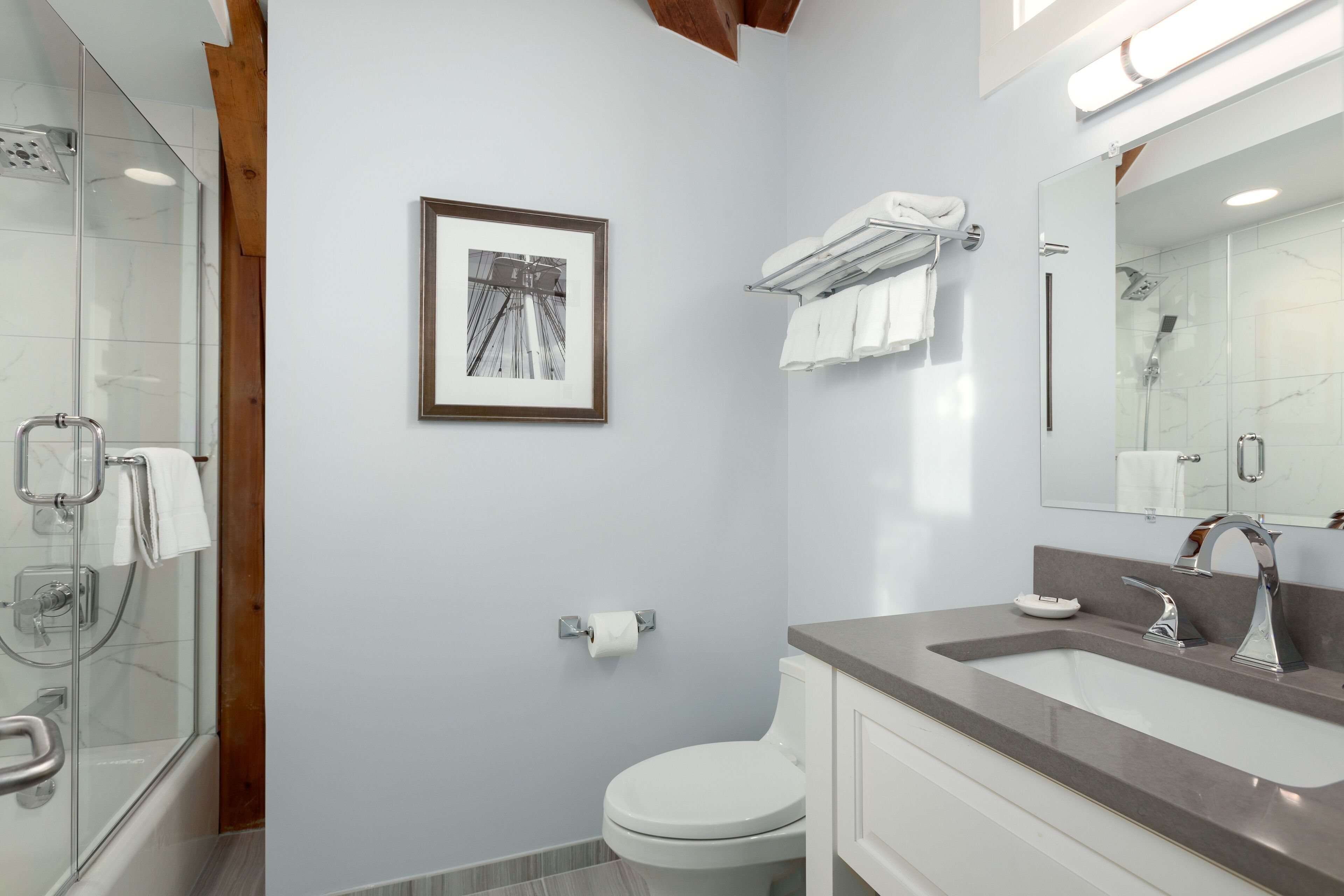 Uma casa de banho moderna com chuveiro de vidro, sanita, lavatório com balatório e um quadro emoldurado na parede.