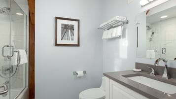Un baño moderno con ducha de vidrio, inodoro, lavabo con tocador y un cuadro en la pared.