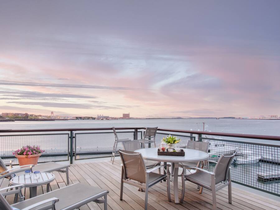 A deck with a table and chairs, overlooking a body of water with a cityscape in the distance.