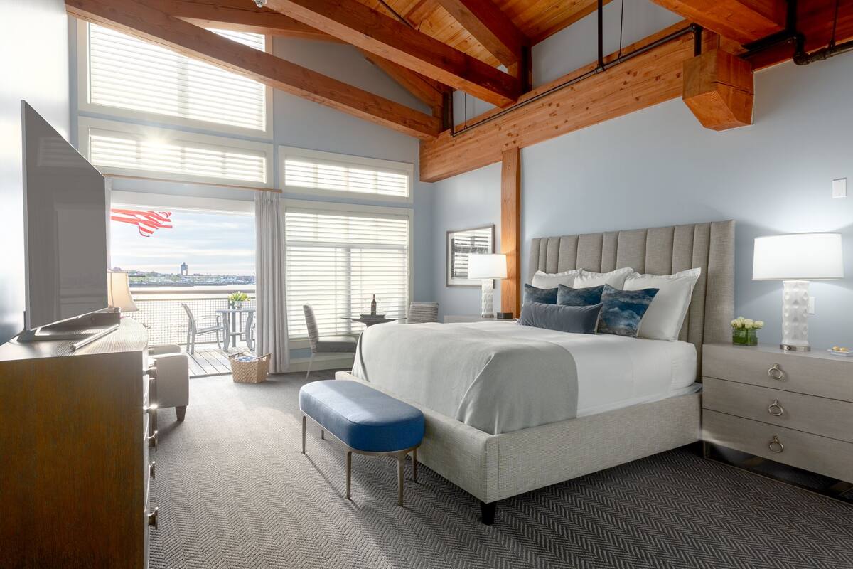 A modern bedroom with a large bed, a desk, and a view of the city through large windows.