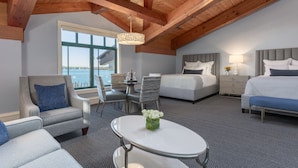 A hotel room with a high ceiling, wooden beams, a large window, a dining area, two beds, and a small table with a vase of flowers. - Boston Yacht Haven Inn & Marina (Boston)