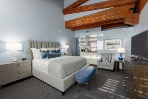 A hotel room with a bed, bedside tables, a desk, a chair, a TV, and a wardrobe.
