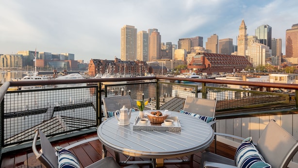 A rooftop terrace with a city skyline view, a round table with chairs, and a tray with a basket and cups. - Boston Yacht Haven Inn & Marina (Boston)