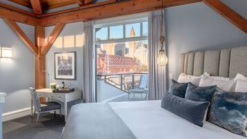 Ein Schlafzimmer mit einem großen Bett, einem Schreibtisch und einem Sessel. Es bietet einen Blick auf eine Stadtansicht durch ein großes Fenster.