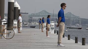 A waterfront promenade with a bridge in the background, a bicycle, and people walking.