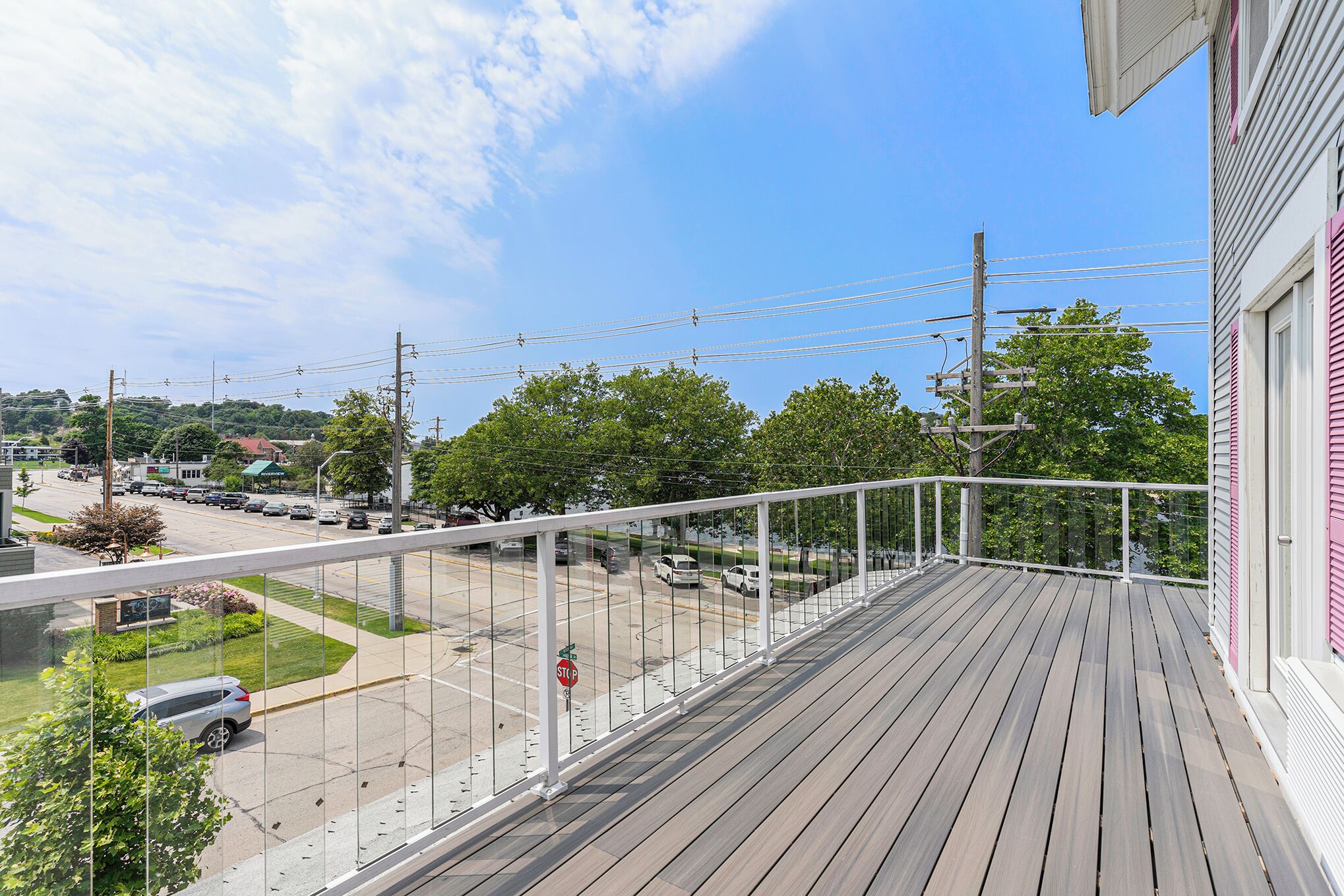 A wooden deck with a white railing overlooking a street with cars and a stop sign.