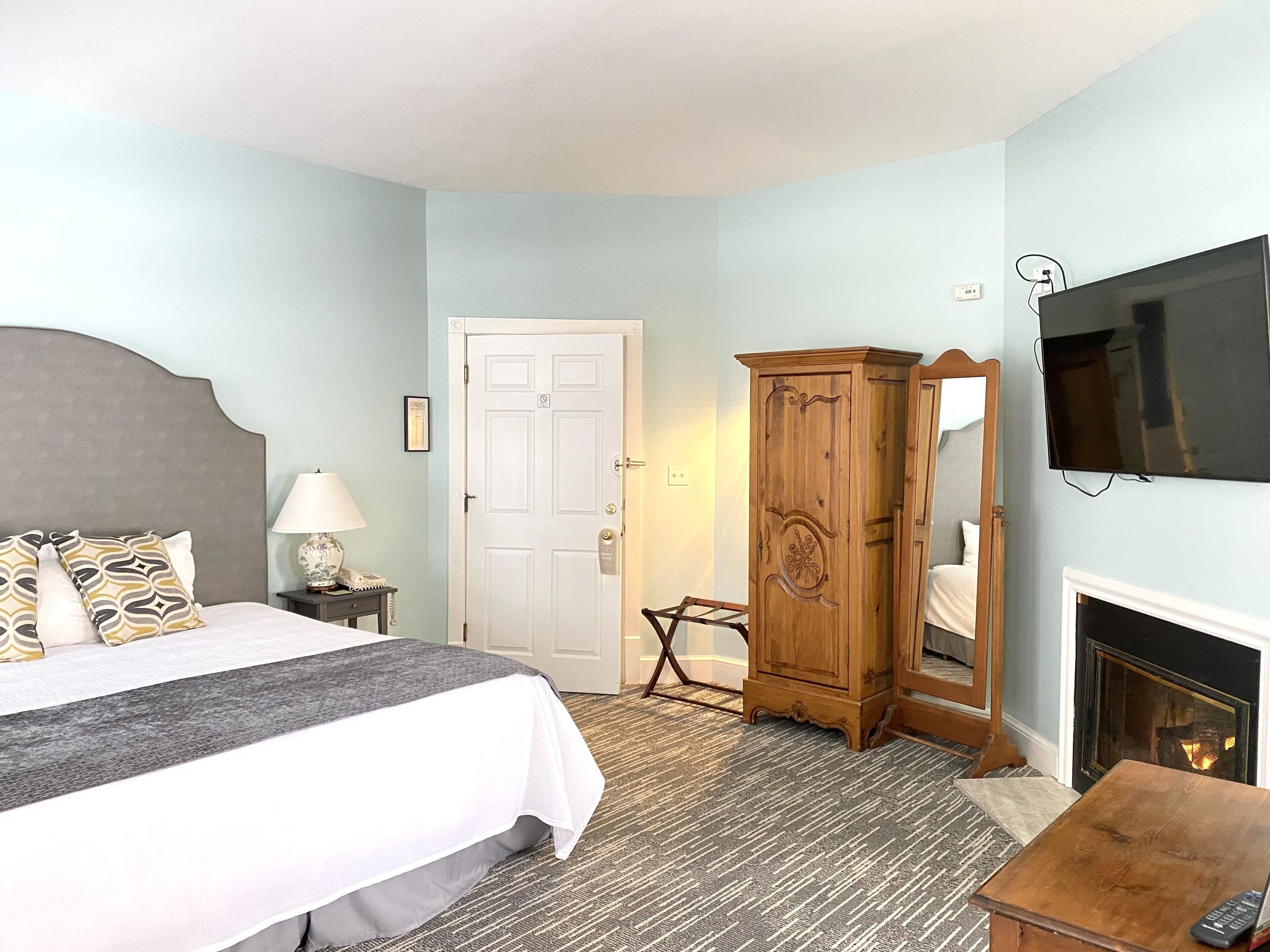 Una habitación de hotel con cama, mesita de noche, lámpara, armario, televisor y chimenea.