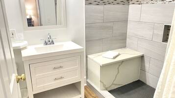 A bathroom with a white vanity, a mirror, a sink, and a shower area with tiled walls.