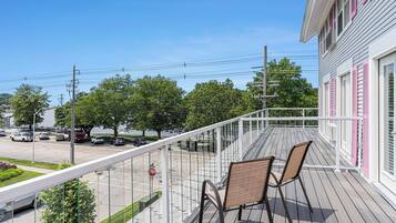 Un balcon avec deux chaises, donnant sur une rue où sont garées des voitures et où se trouve un panneau de signalisation.
