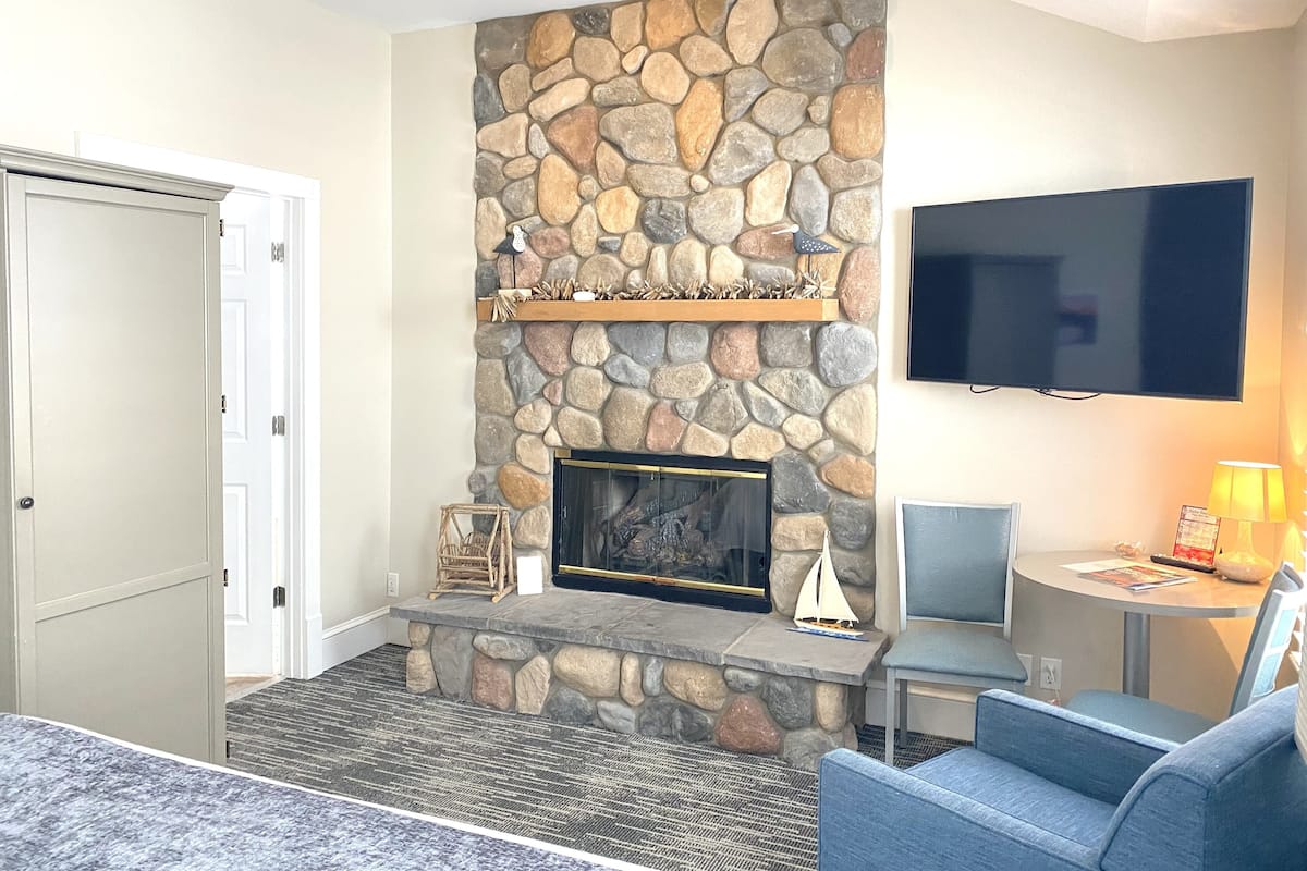 Una sala de estar con chimenea de piedra, un televisor de pantalla plana y una zona de estar con un sofá azul y una mesita.