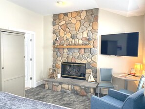 A living room with a stone fireplace, a flat-screen TV, and a seating area with a blue sofa and a small table.