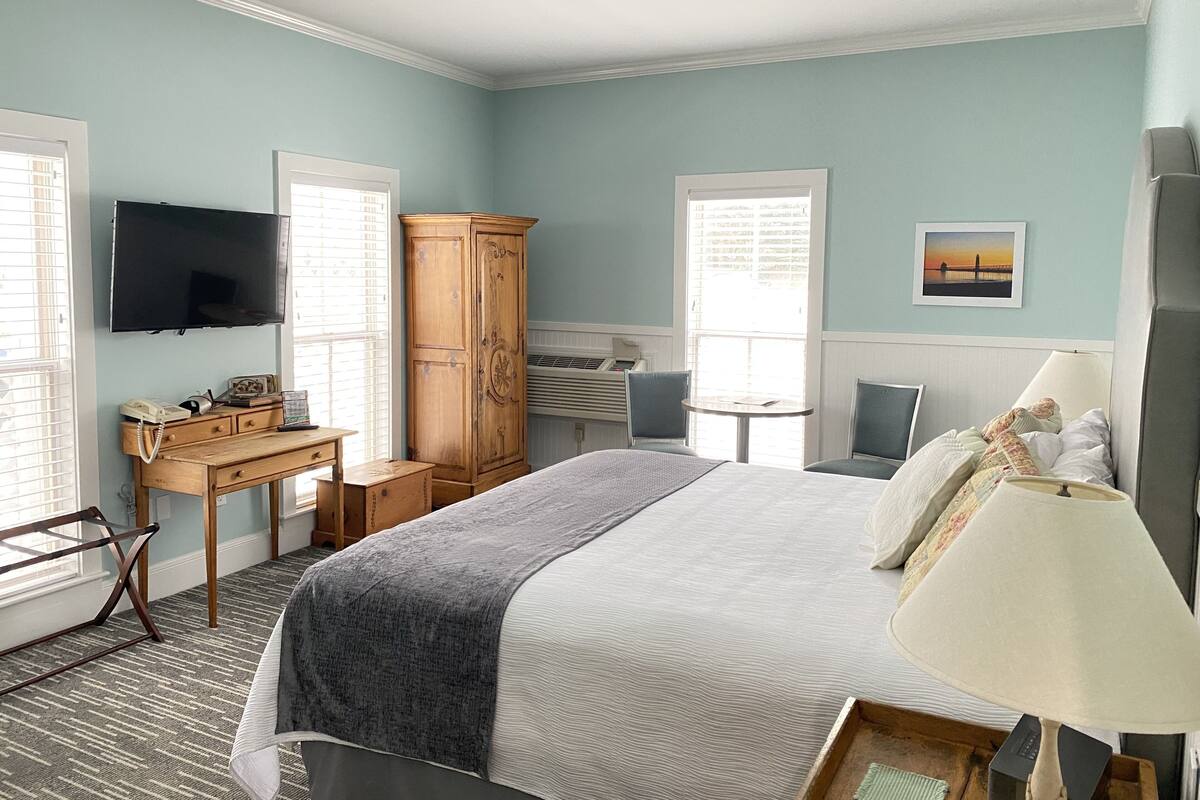 Un dormitorio con cama, mesita de noche, lámpara, televisión, armario, escritorio, silla y ventana con persianas.