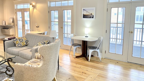 A spacious living room with a grey sofa, a small table with a lamp, and a view through large French doors. - Harbor House Inn (Grand Haven)