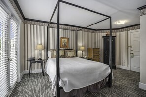A four-poster bed with a canopy, a bedside table with a lamp, a dresser, and a framed picture on the wall. - Harbor House Inn (Grand Haven)