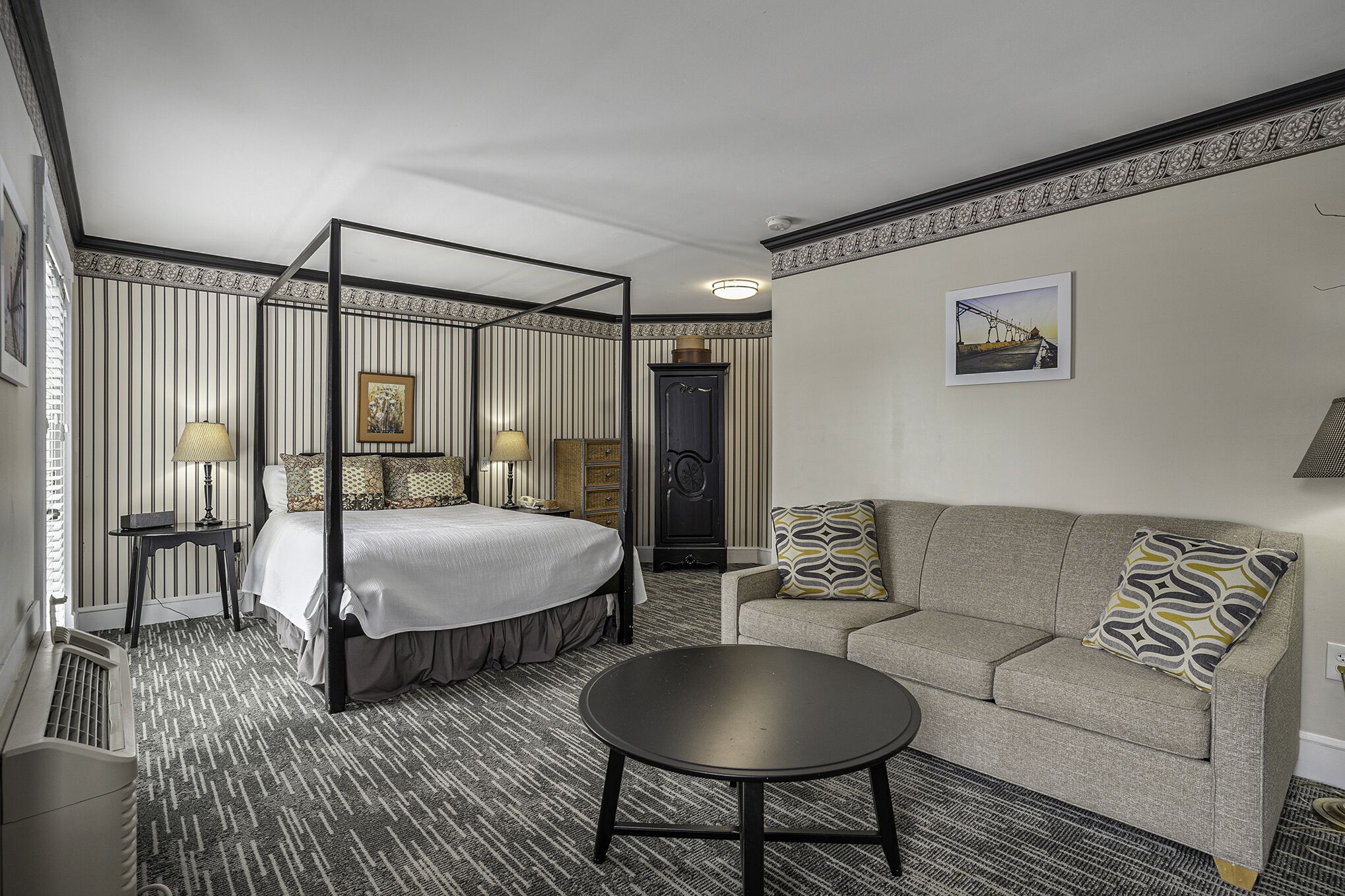 A hotel room with a four-poster bed, a sofa, a round coffee table, and a patterned carpet.