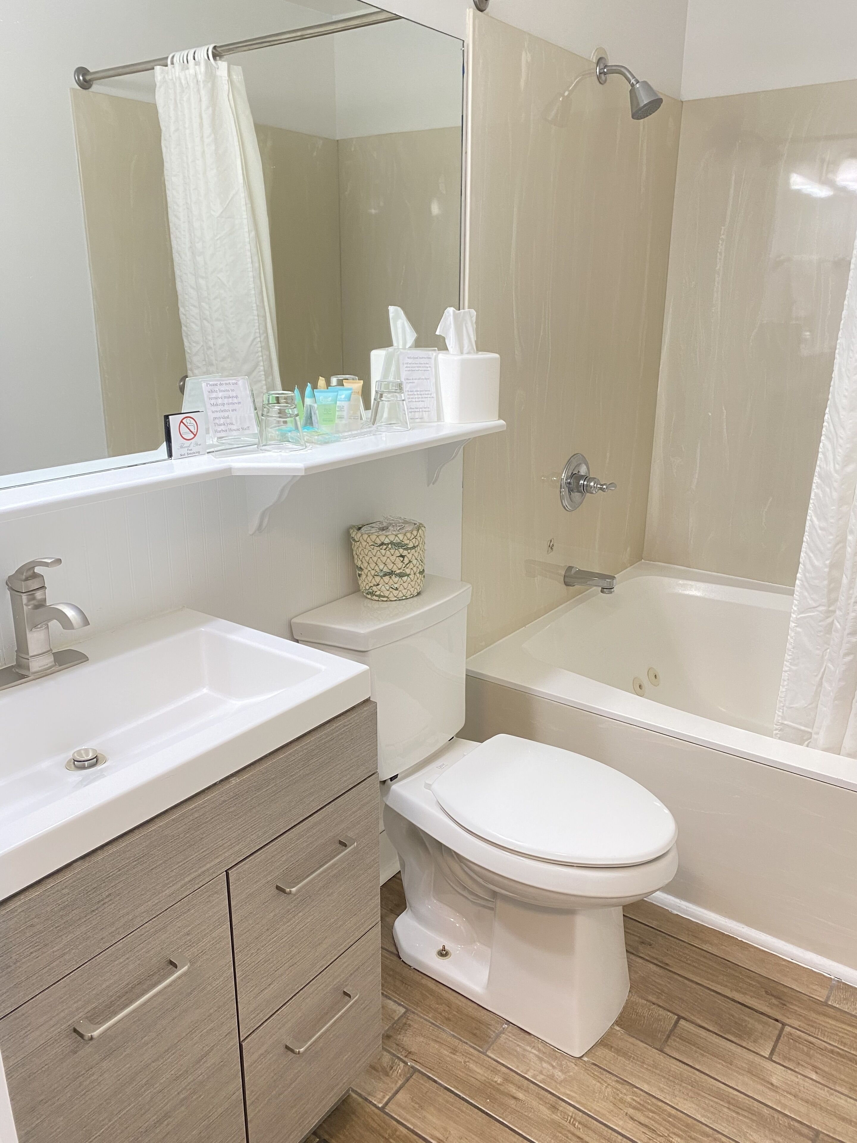 Une salle de bain moderne avec un lavabo, des toilettes et une baignoire. On trouve des articles de toilette sur une étagère au-dessus des toilettes.