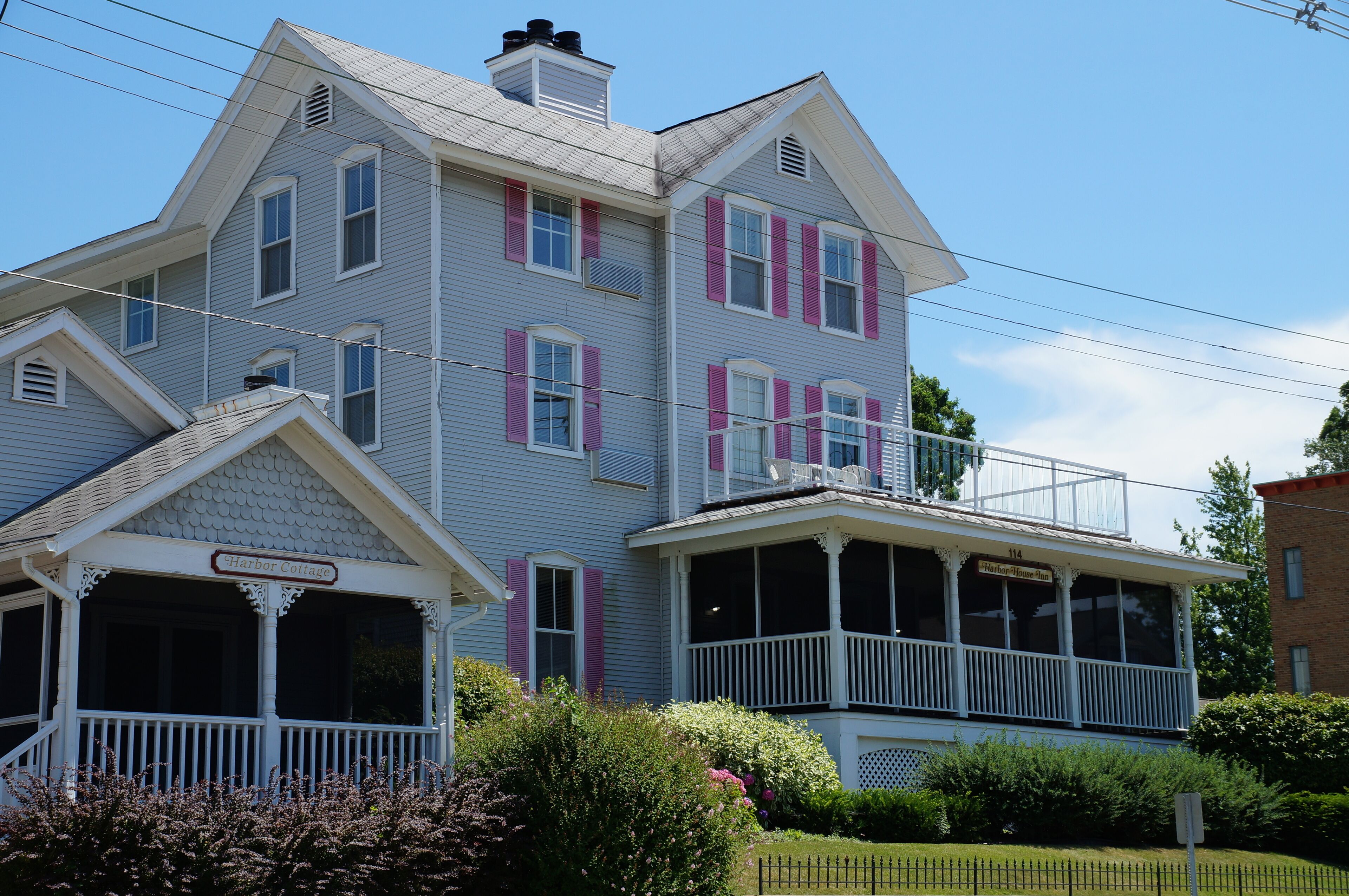 Uma casa de dois andares com varanda e sacada, identificada como 'Harbor Cottage'.