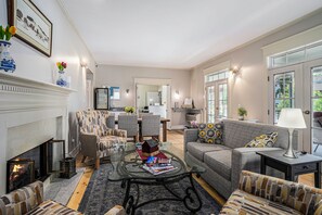 A living room with a fireplace, a sofa, armchairs, a coffee table, and a dining area in the background. - Harbor House Inn (Grand Haven)