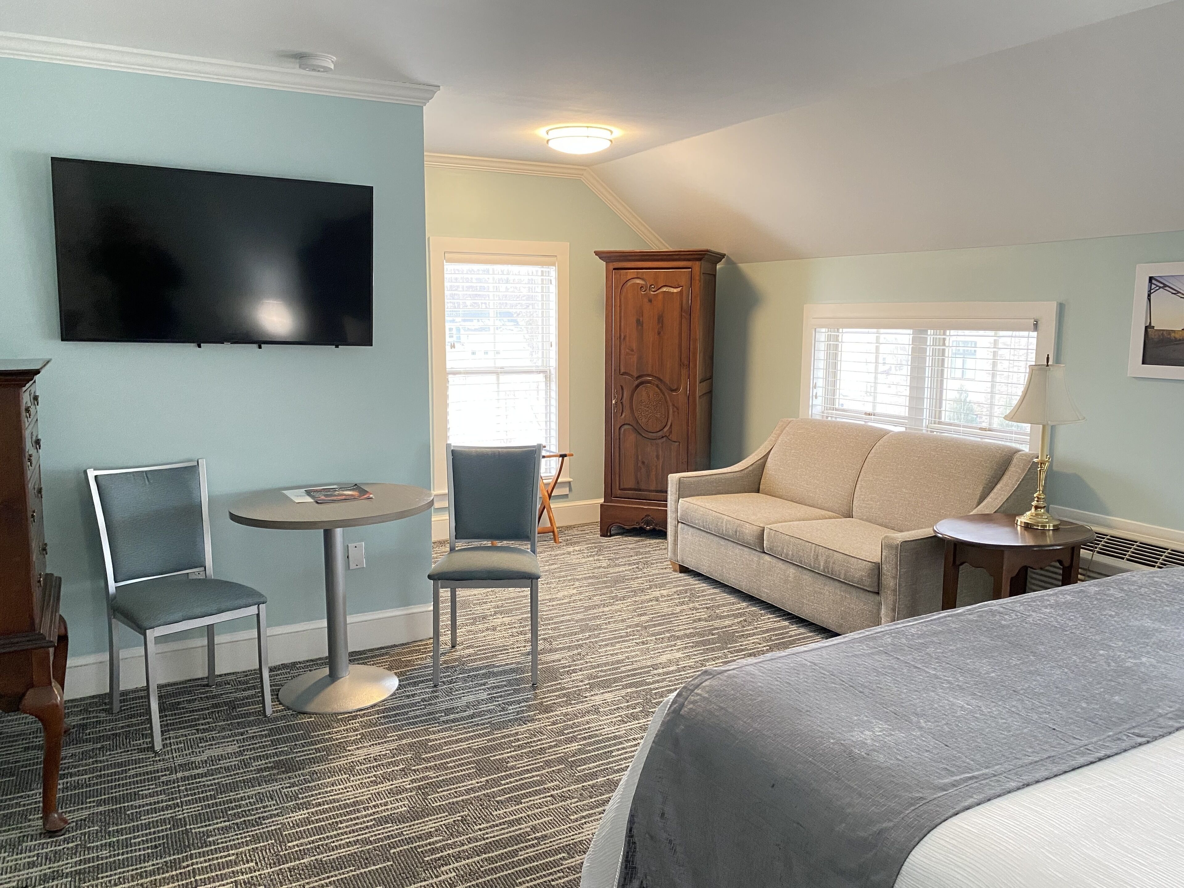 A hotel room with a bed, a TV, a sofa, two chairs, a small table, and a cabinet.