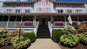 A two-story building with a porch, steps leading to the entrance, and flags on either side. - Harbor House Inn (Grand Haven)