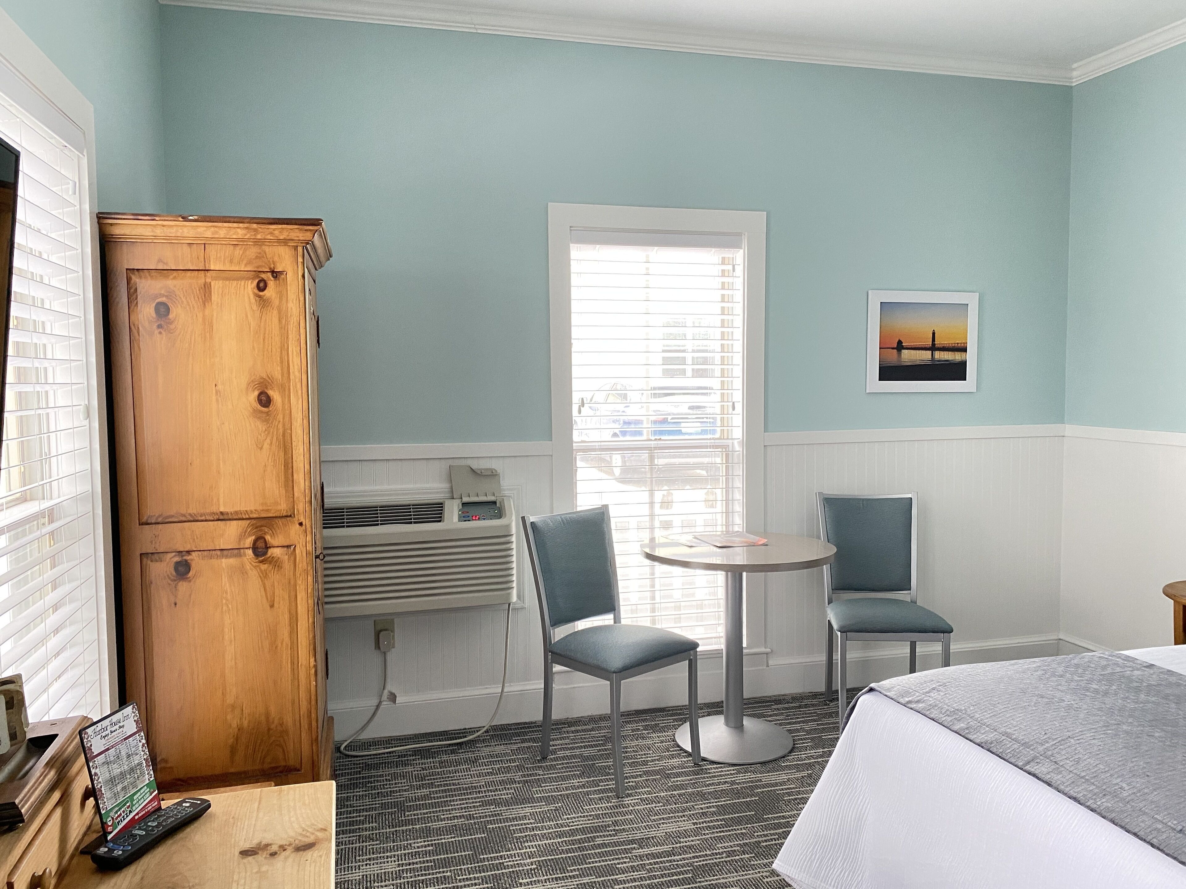 Habitación de hotel con una cama, dos sillas, una mesita, un armario de madera y una ventana con persianas.
