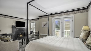 A hotel room with a large bed, a television, a fireplace, a desk, and a chair. - Harbor House Inn (Grand Haven)