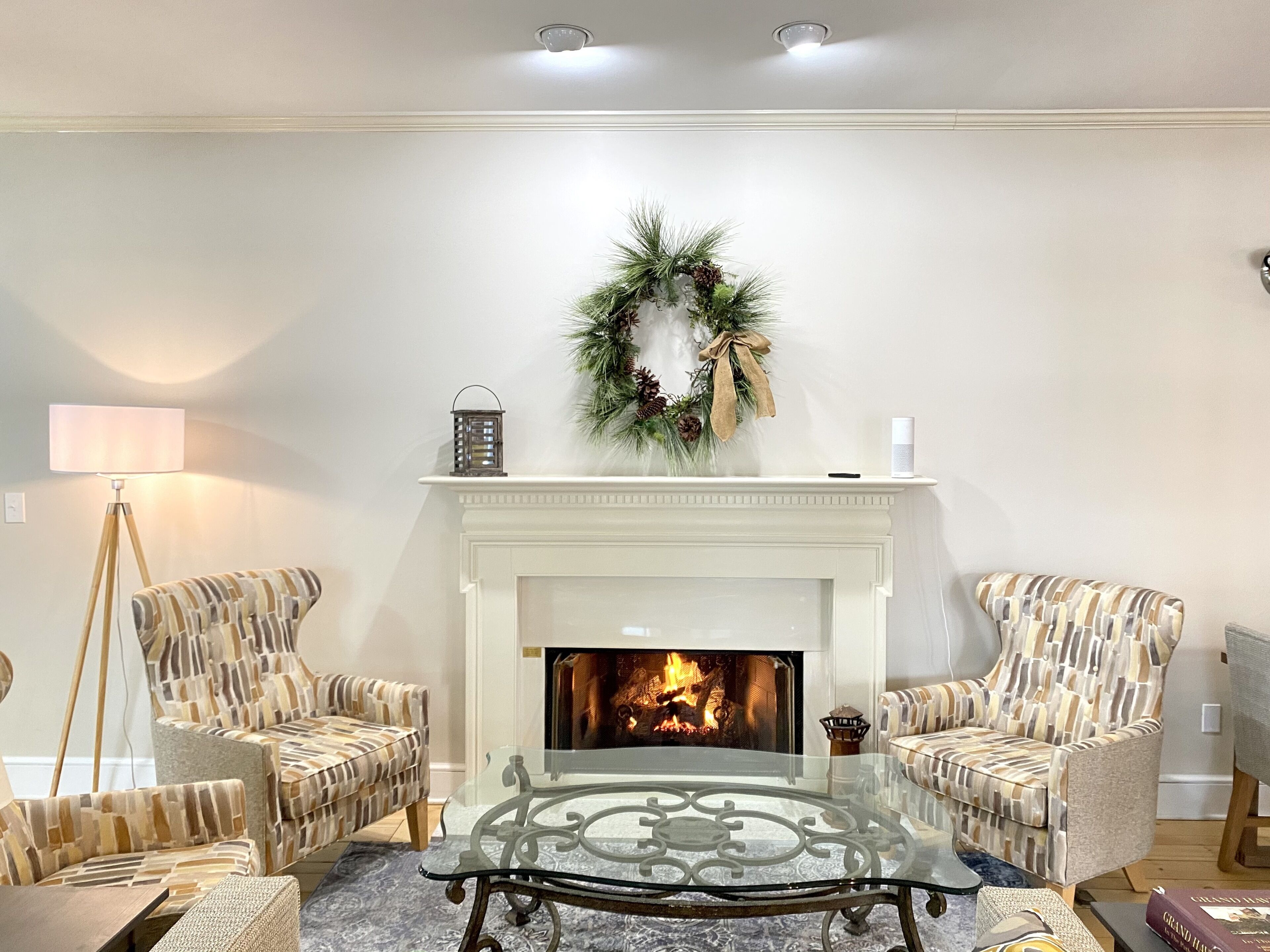 Un salon avec une cheminée, deux fauteuils à motifs, une table basse en verre et un lampadaire.