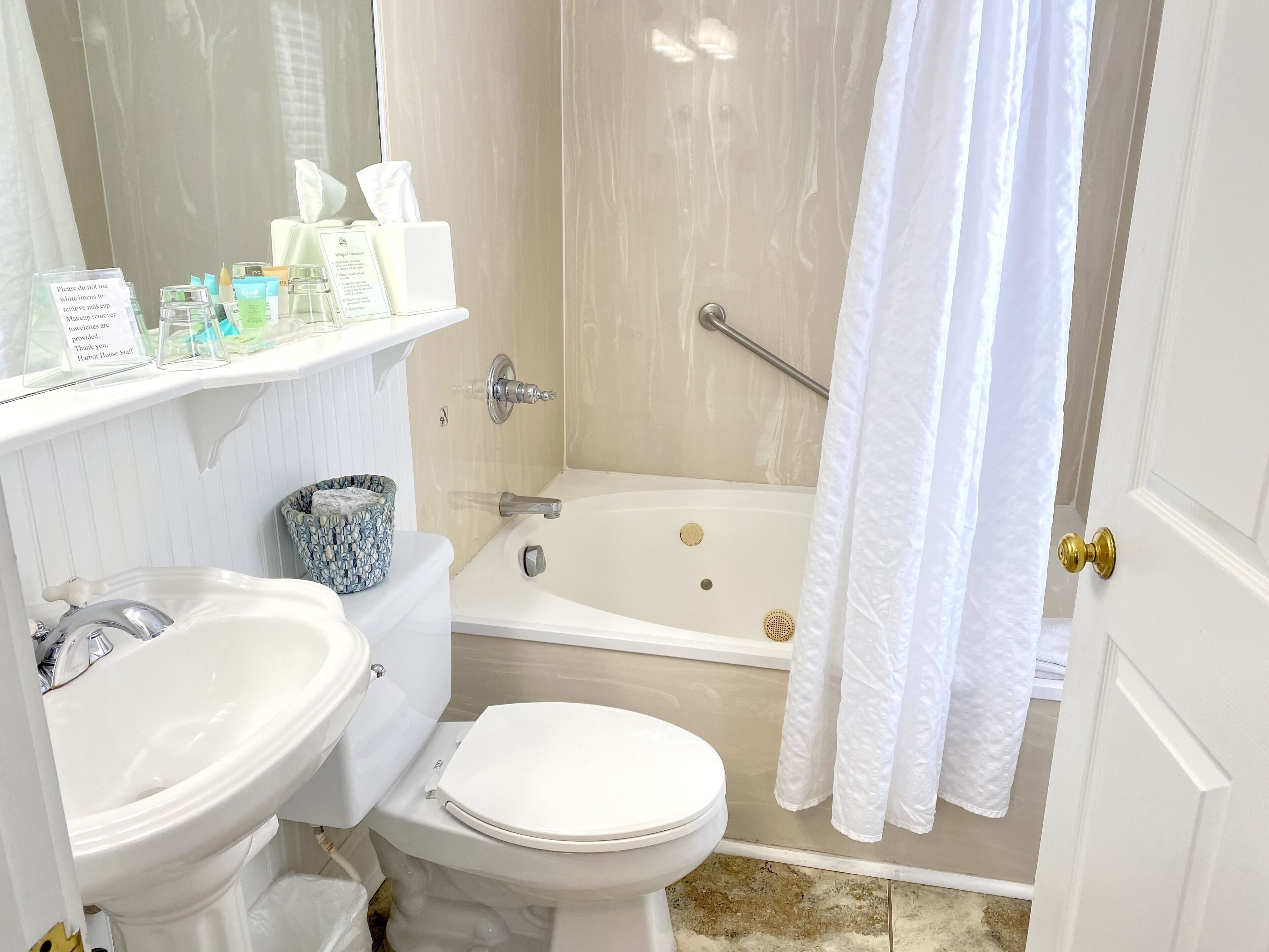 Een badkamer met toilet, wastafel en bad. Toiletartikelen staan op een plankje en het douchegordijn is gedeeltelijk open.