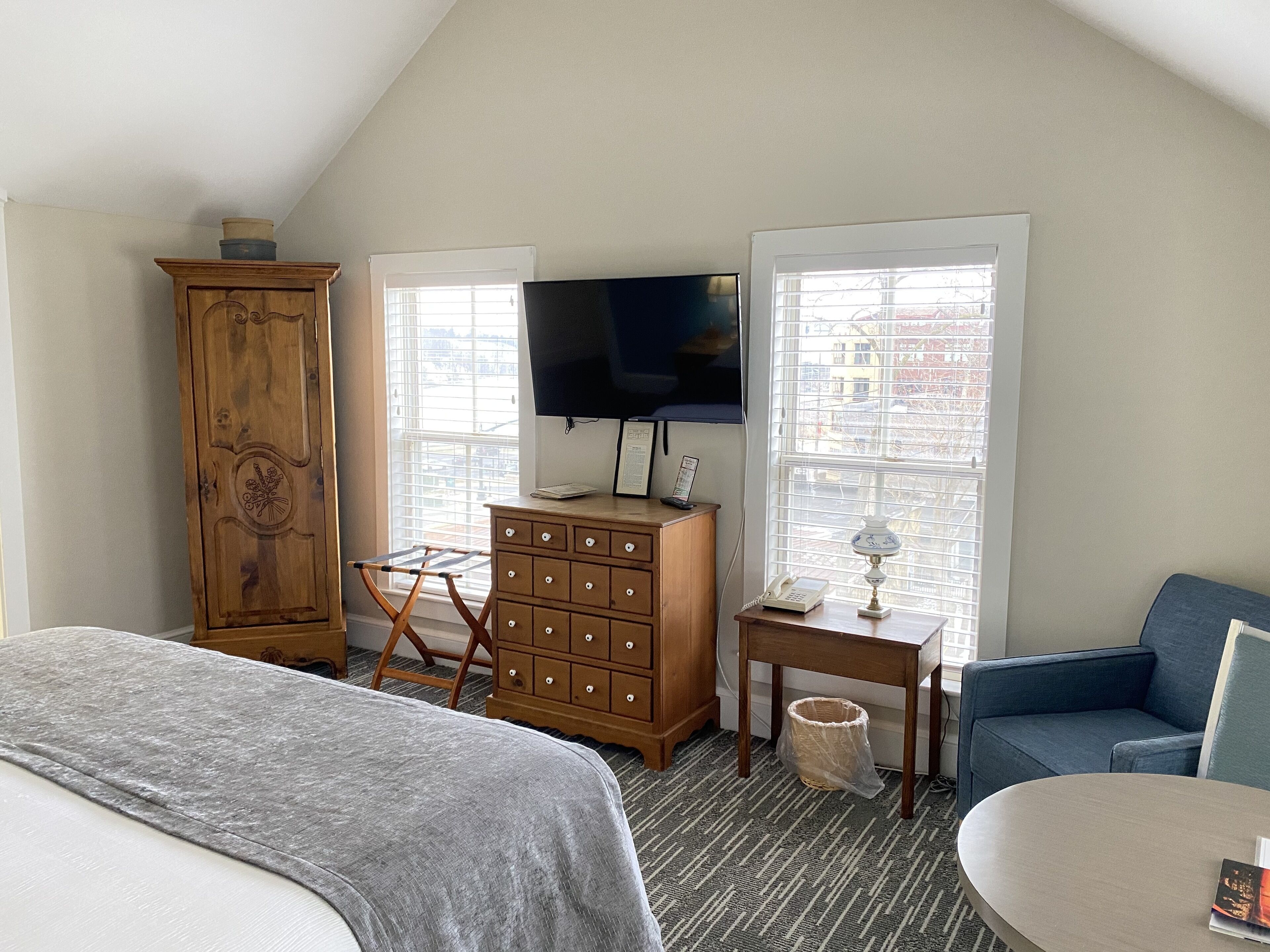 A bedroom with a bed, a dresser, a TV, a chair, and a window with blinds.