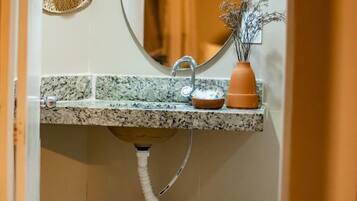 A bathroom with a granite countertop sink, a round mirror, a straw hat, and two woven baskets.