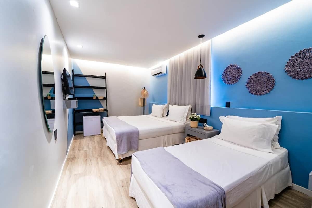 A modern hotel room with two beds, a small kitchenette, a mirror, and decorative wall art.