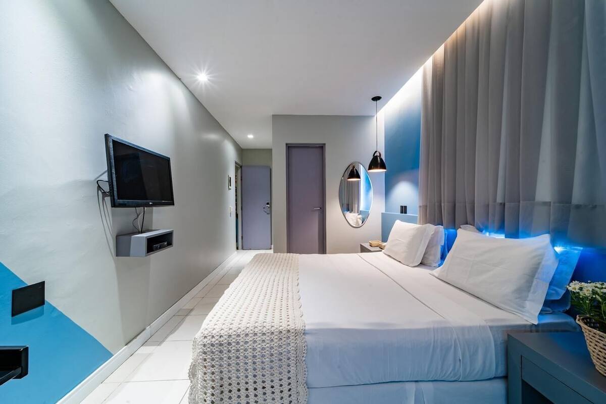 A modern bedroom with a large bed, a mounted TV, and a bedside table with a lamp.