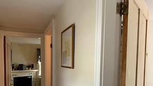 A hallway with wooden flooring, white walls, and a door leading to a kitchen area. - Youngtown Inn & Restaurant (Lincolnville)