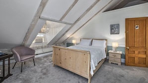 A bedroom with a sloped ceiling, a wooden bed, a chair, a nightstand, a lamp, and a door. - Youngtown Inn & Restaurant (Lincolnville)