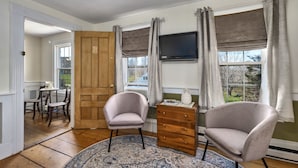 A room with a wooden door, a television mounted on the wall, two armchairs, a wooden dresser, and a patterned rug. - Youngtown Inn & Restaurant (Lincolnville)