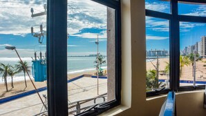 Vista de una playa desde el interior de un edificio, con cielo despejado y un horizonte urbano distante.