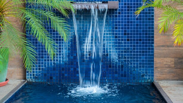 Pared azul con azulejos, una cascada y una piscina.
