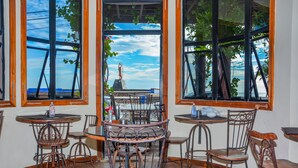 Un restaurante con sillas y mesas de metal rústico, ventanas amplias con vista al cielo y una estatua.