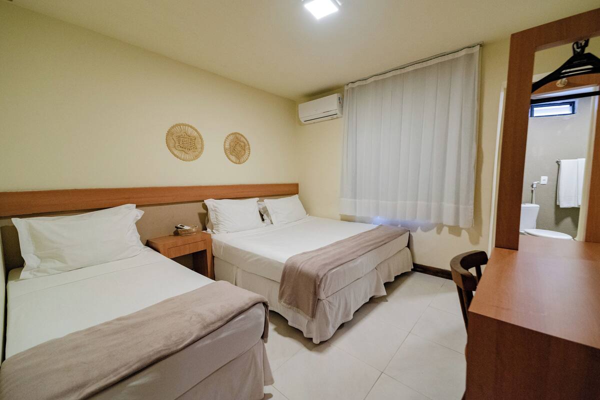 Une chambre d’hôtel avec deux lits, une tête de lit en bois, une table de chevet, un bureau et un miroir.