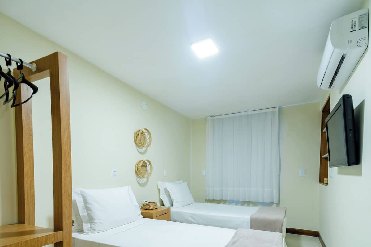 Une chambre d’hôtel avec deux lits, une chaise en bois, une télévision et un climatiseur.