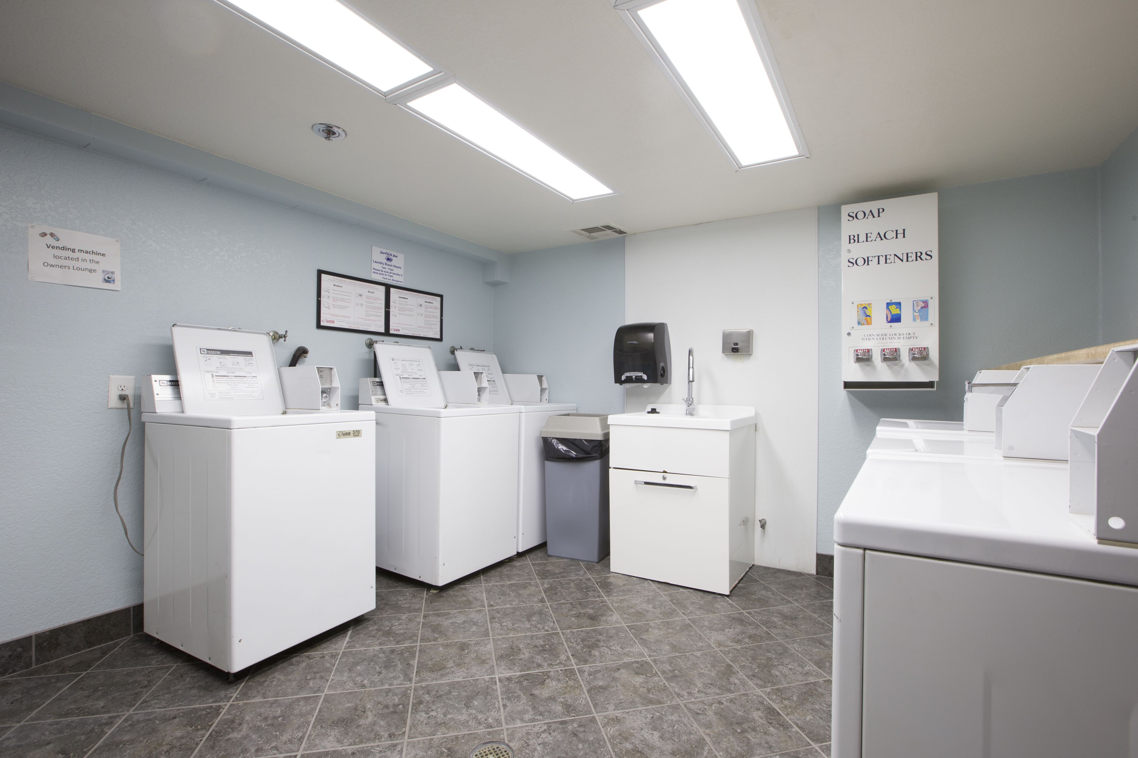 Une buanderie équipée de plusieurs machines à laver, d’une poubelle et d’un distributeur de savon.
